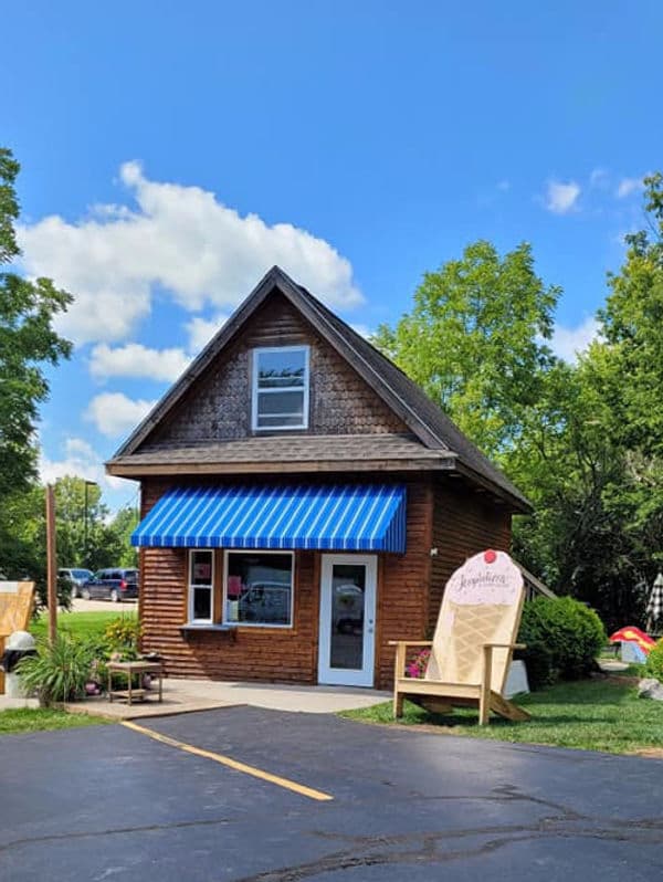A quaint wooden building with a blue-striped awning and a sign, surrounded by lush greenery and a clear blue sky.