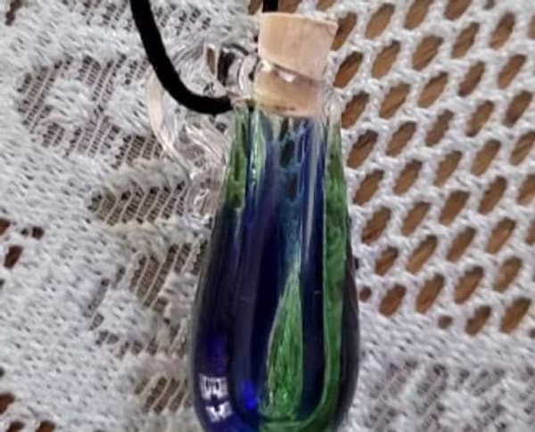 A small, glass vial with blue and green swirls, sealed with a cork and hung on a black cord.